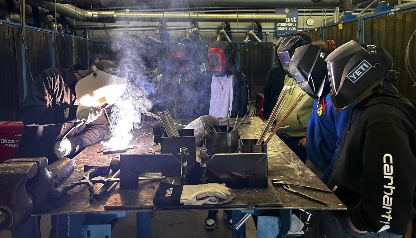 Student welding with other students watching